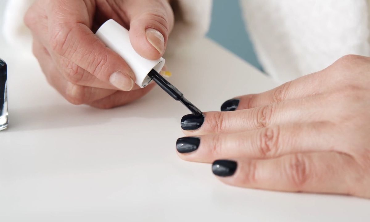 devojka nanosi crni lak na nokte
